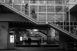 Personnages sur un quai de gare on voit la gare en haut - Photo en noir et blanc